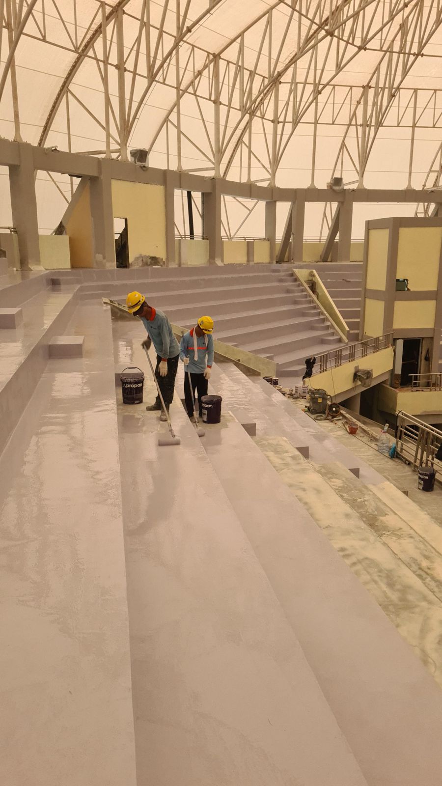 Dua aplikator mengaplikasikan lapisan pelindung pada area tribun beton menggunakan roller