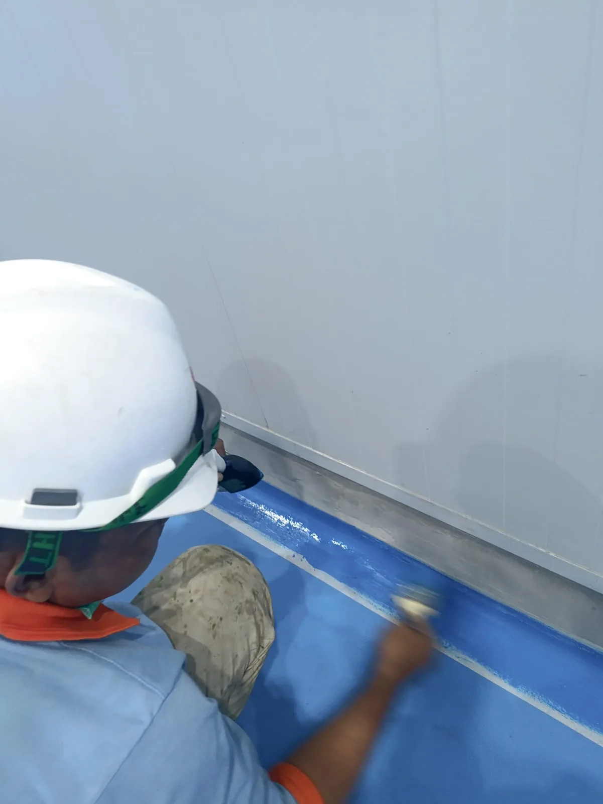 Proses pelapisan epoxy berwarna biru pada pertemuan lantai dan dinding