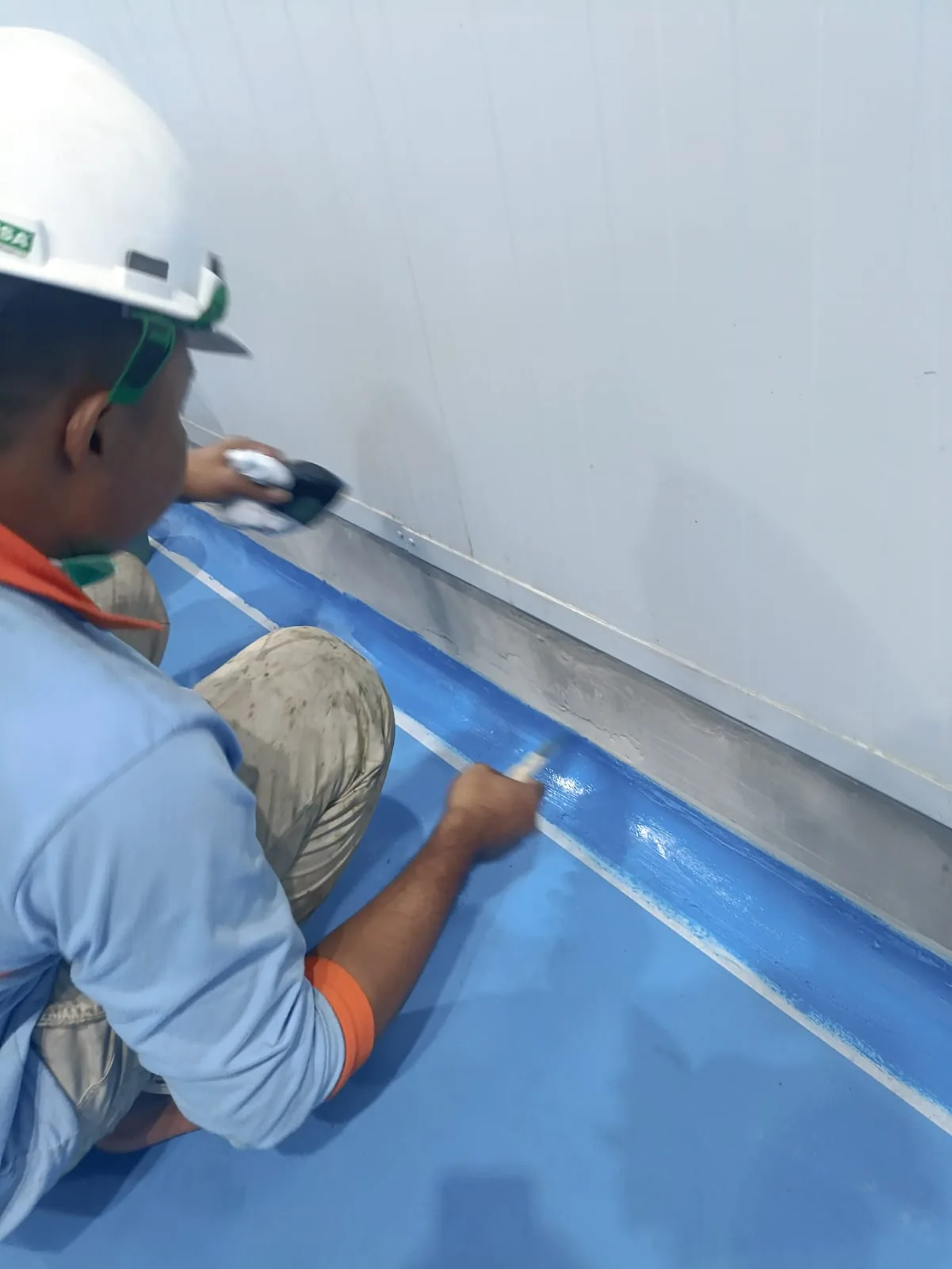 Tahap pengerjaan coating epoxy pada garis pertemuan dinding dan lantai pabrik