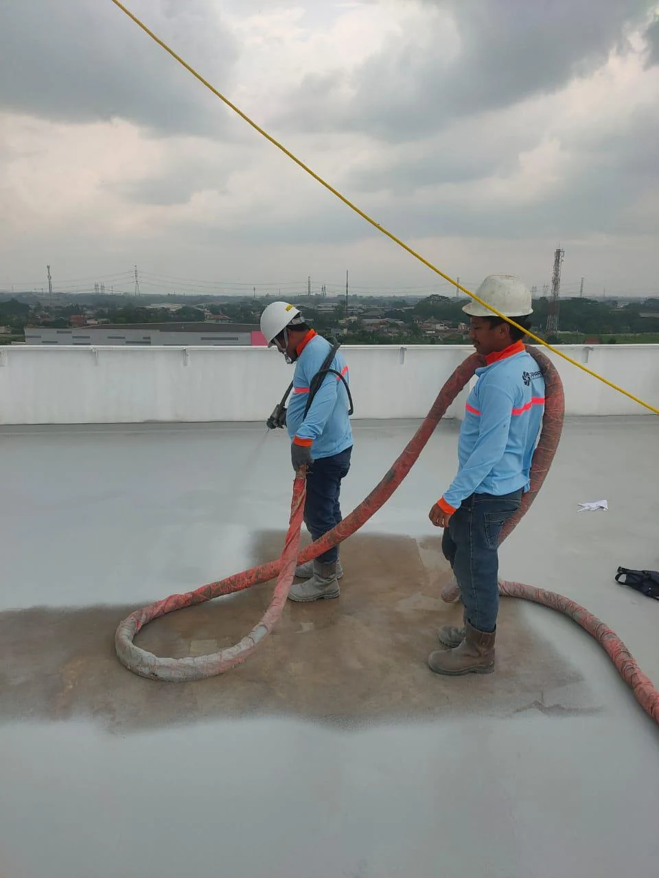 Pekerja melakukan aplikasi pelapis atap pabrik menggunakan peralatan spray